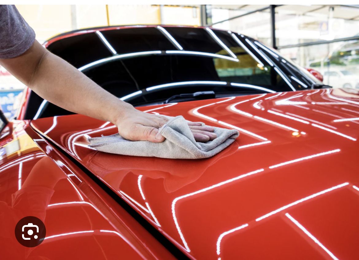 A person is cleaning the hood of a red car.