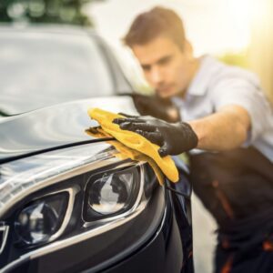 A man in black shirt cleaning car 's hood.