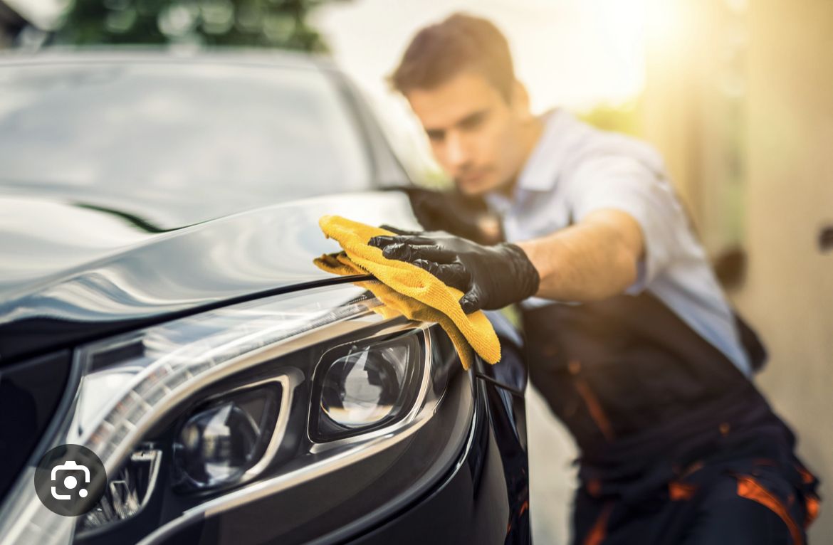 A man in black shirt cleaning car 's hood.