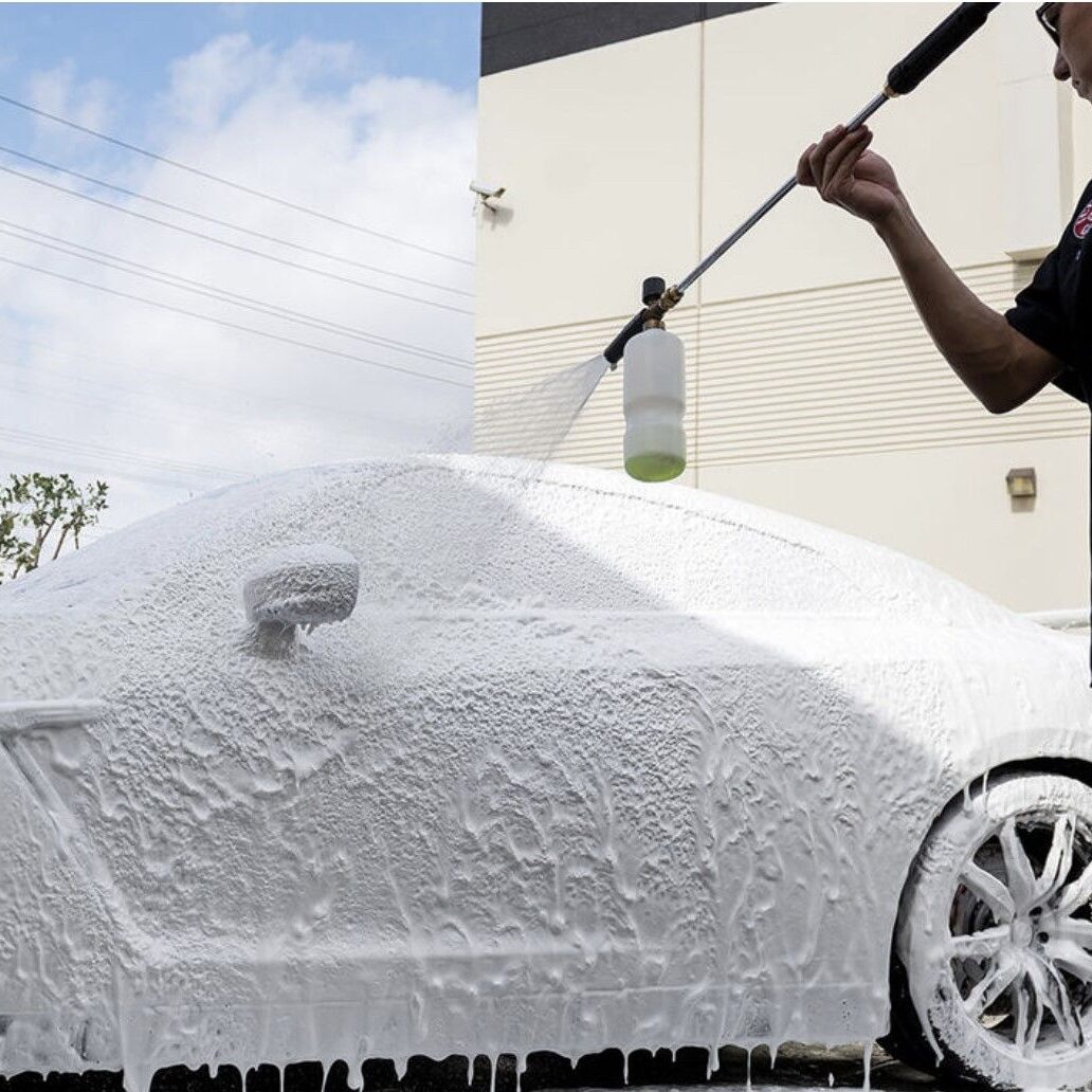 A man is washing his car with a hose.